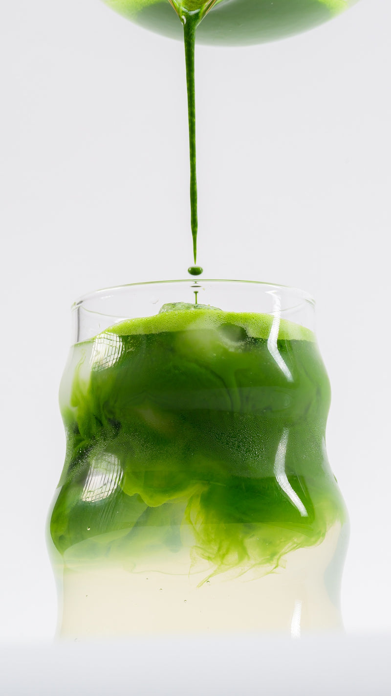 Green matcha being poured over ice into a clear glass.