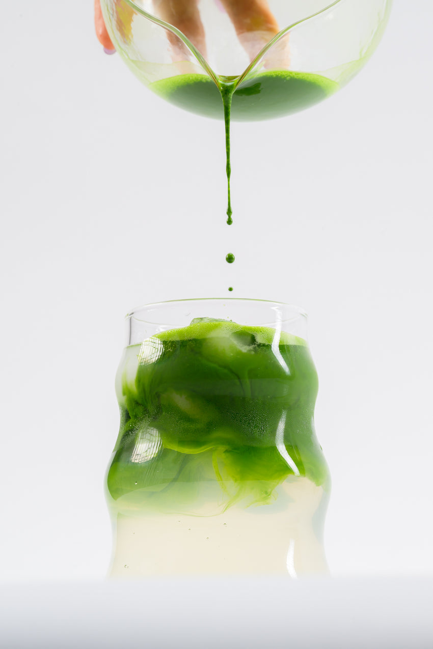 Matcha being poured into an iced latte in a clear glass.
