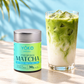 Tall slim Yōko Matcha 30g ceremonial matcha tin with a plain silver lid beside an iced matcha latte